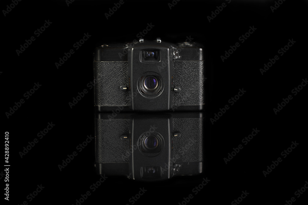 The old very popular automatic film camera on black glass background with reflection.