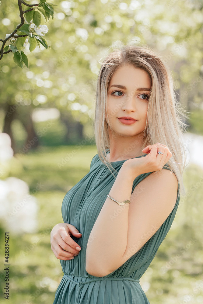 Fashion portrait of beautiful woman with short blonde hair in green dress posing in blossom spring garden Fashion portrait of beautiful woman with short blonde hair in green dress posing in blossom spring garden