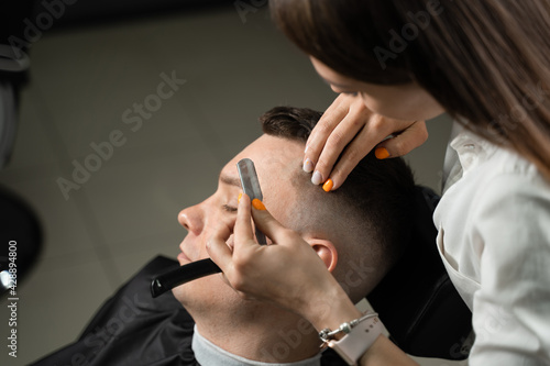 Straight razor cut man hair in barbershop. Attractive woman barber making hairstyle for handsome man.
