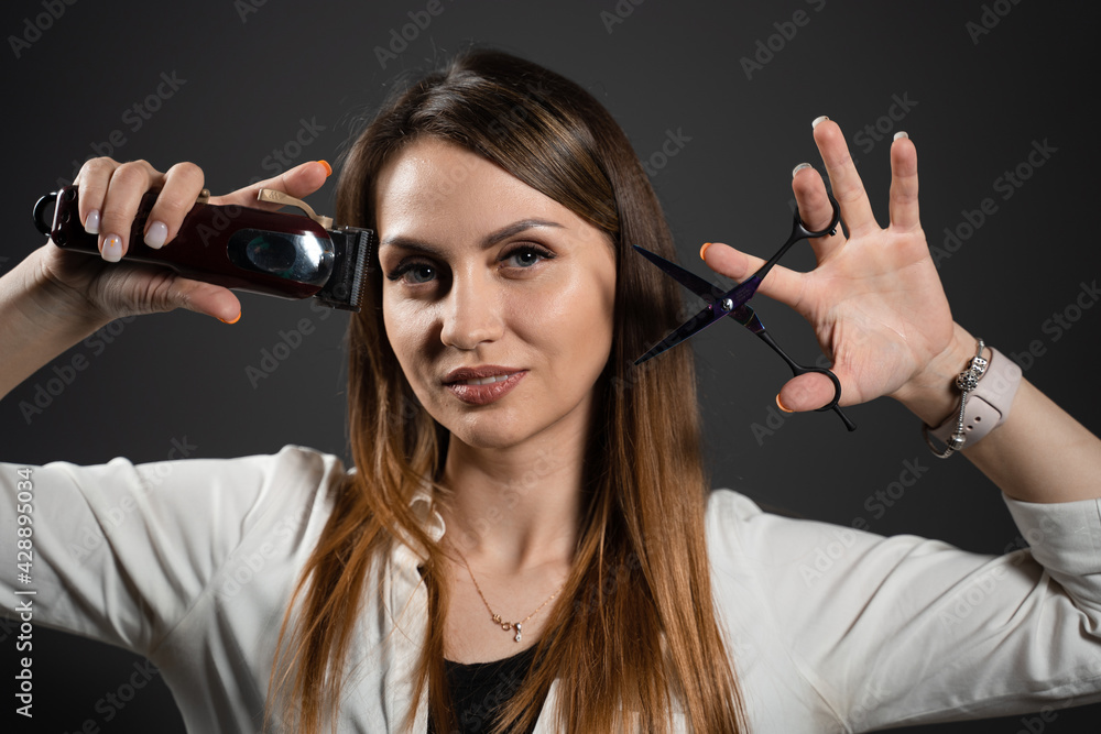 Woman barber with scissors and hair clipper in barbershop. Portrait of hairdresser for advert.