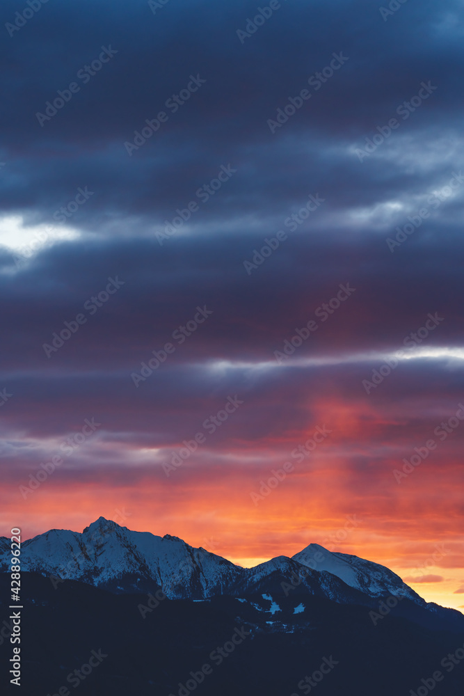 Alpine mountains with snow tops at sunset with dramatic red colored stormy cloudscape in Tirol, Austria