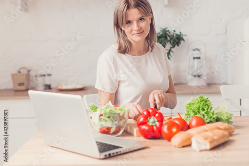 Woman cutting vegetables on salad and view recipes in laptop on kitchen.