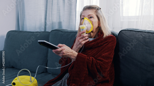 Elderly woman using oxygen mask while changing channels on tv at home. High quality photo