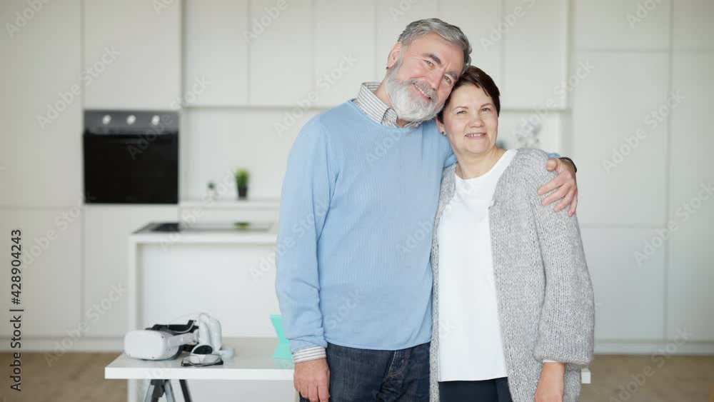 Middle shot of happy loving senior couple posing indoors at home. Cheerful handsome man and beautiful woman hugging looking at camera and smiling. Eternal love concept Middle shot of happy loving senior couple posing indoors at home. Cheerful handsome man and beautiful woman hugging looking at camera and smiling. Eternal love concept