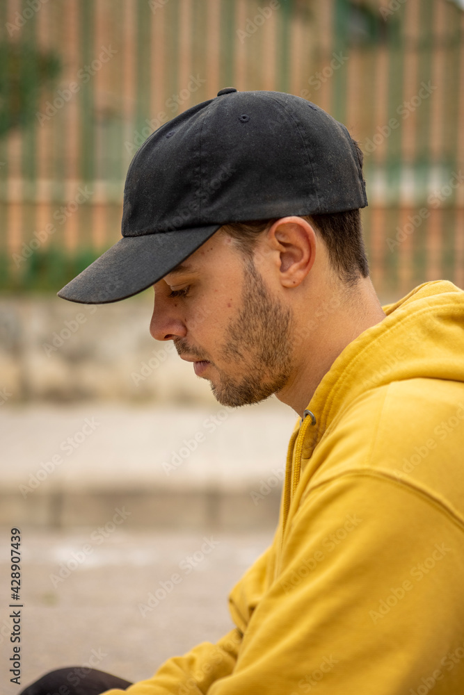 Portrait of a young male wearing a yellow hoodie and black cap in a street