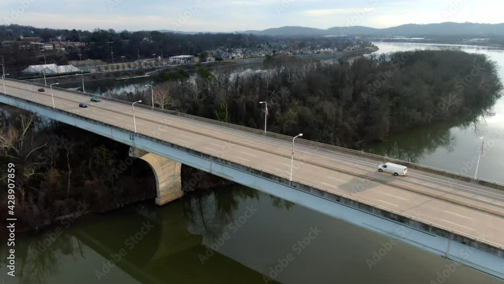 Highway bridge over calm river and island with bare trees in winter. Traffic on interstate crossing waterway. Travel, tourism, transportation and industry concept. Aerial view, drone slide left. Highway bridge over calm river and island with bare trees in winter. Traffic on interstate crossing waterway. Travel, tourism, transportation and industry concept. Aerial view, drone slide left.