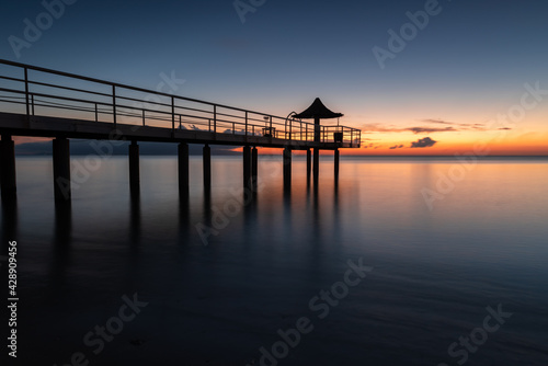 Incredible long exposure of a pier with a vanishing point perspective. Wharf with some colums over the smooth sea. Pastel tones of orange, yellow, blue and pink. © Renata Barbarino