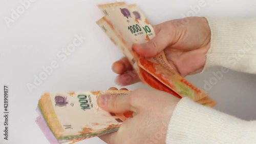 Caucasian woman's hand counting extended banknotes of Argentine pesos in close-up and on white background