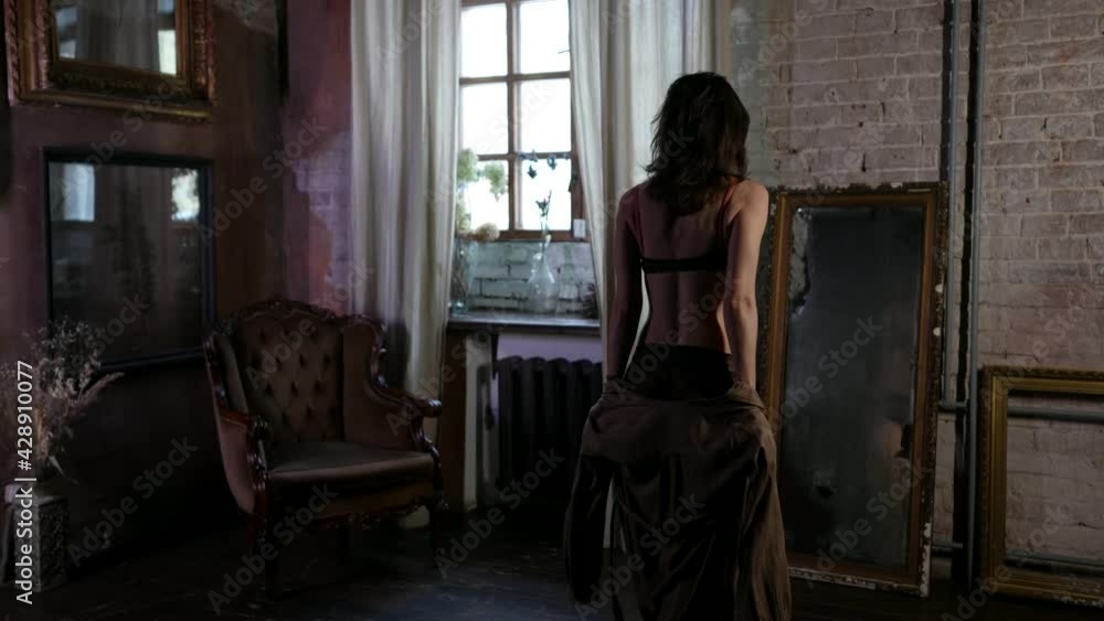 sexy lady in lingerie is viewing herself in old vintage mirror in living room