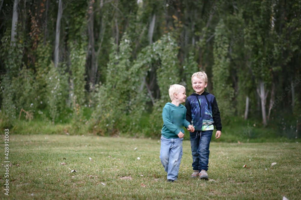 Happy little boys walking together in lush green outdoor setting. Brothers having fun in the outdoors.