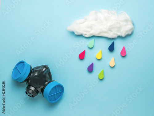 A gas mask and a cloud with falling multicolored drops on a blue background. Spraying and protection against toxic substances. Climate picture. photo