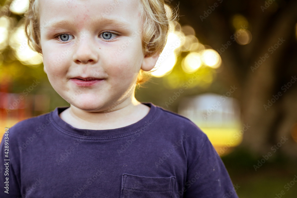 Little boy with blonde curly hair playing in the park at sunset Little boy with blonde curly hair playing in the park at sunset