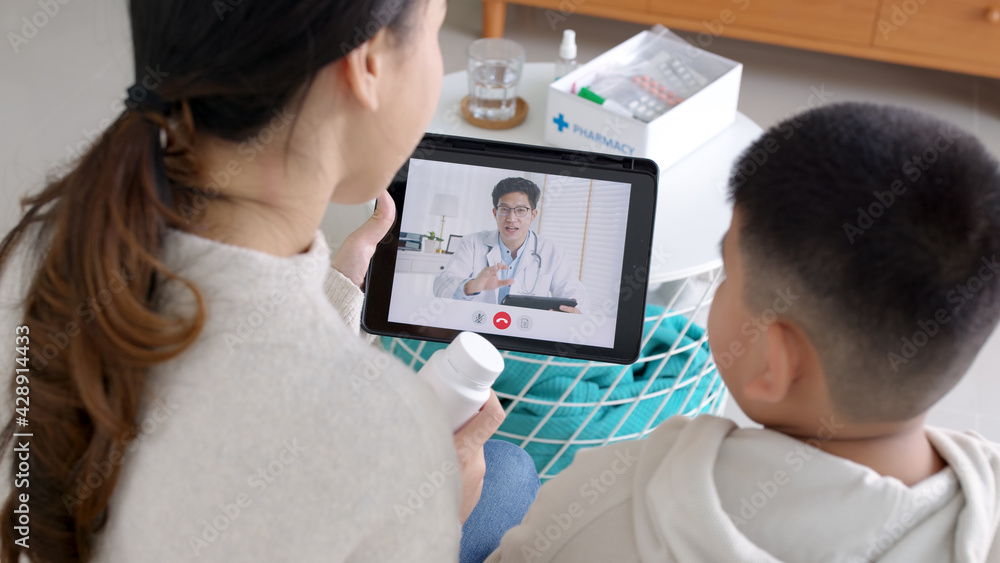 Over shoulder view of young asia parents and son talk to doctor on cellphone videocall conference medical app in telehealth telemedicine online service hospital quarantine social distance at home. Over shoulder view of young asia parents and son talk to doctor on cellphone videocall conference medical app in telehealth telemedicine online service hospital quarantine social distance at home.