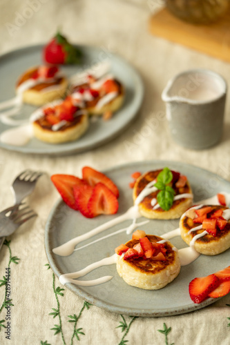 Cottage cheese cakes with strawberries and sour cream on plates. Breakfast table. High quality photo. Top view
