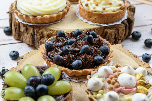 Closeup of pie with buttery dough stuffed with chocolate ganache, decorated with mertilos. On a wooden plate and surrounded by other pies (side view). photo