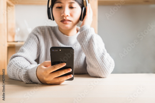 young woman in casual wear sitting listening to music on a smartphone with a white headphone in home office