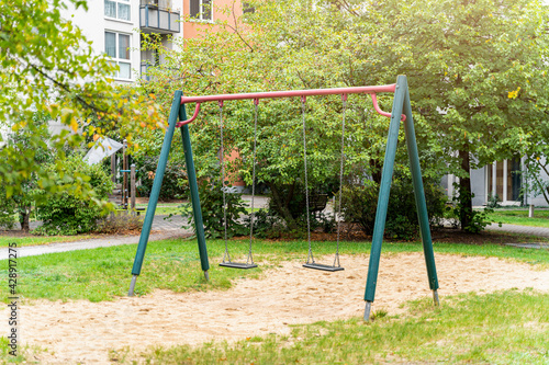 Modern multi-colored playground with slides, swings and other children's attractions on the sand in the courtyard with green trees on a summer day