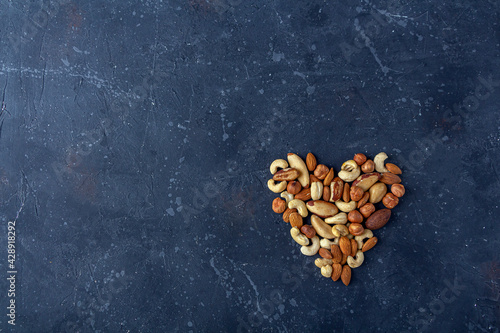 Heart from various types of nuts on dark background. Cashew, hazelnuts, almonds and Brazil nuts top view. Healthy vegetarian snacks. Protein-containing food. Flat lay, copy space.
