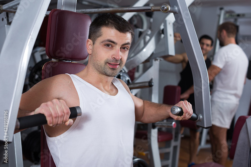 Muscular man doing strength training on fitness machine in modern gym