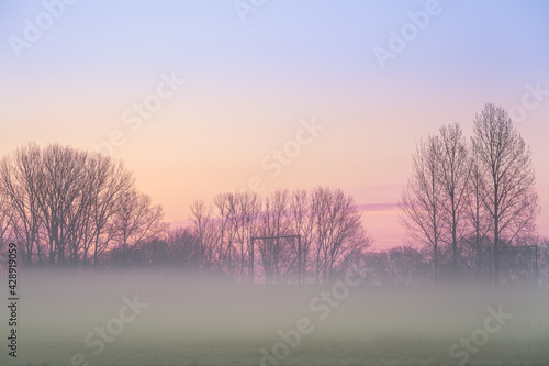 fog over the grassland with in the background a railway with electric top mast
