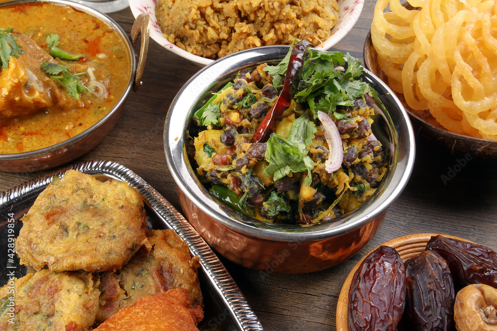 Bengali Iftar Ramadan breakfast spread ripe dates peep fried spicy piaju onion fitter eggplant tanpura potato chop haleem jilapi khichuri rice chana sola curry on rustic wooden table