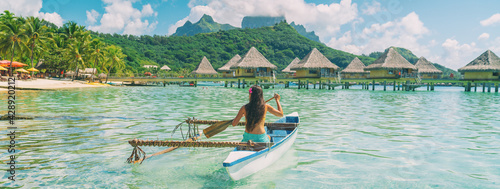 Bora Bora travel vacation iconic photo. Outrigger Canoe - woman paddling in traditional French Polynesian Outrigger Canoe. Mount Otemanu and overwater bungalow resort hotel sport lifestyle