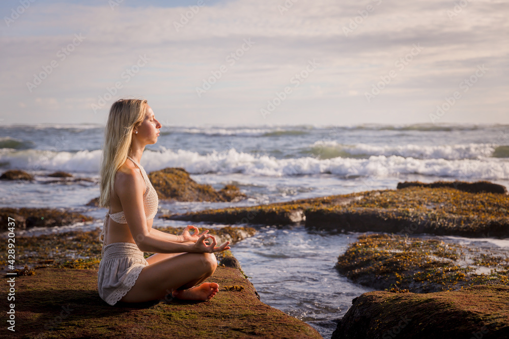 Woman practicing yoga on the beach. Sitting in Padmasana, Lotus Pose. Hands in gyan mudra. Positive energy. Healthy life concept. Yoga retreat. Copy space. Beach in Bali