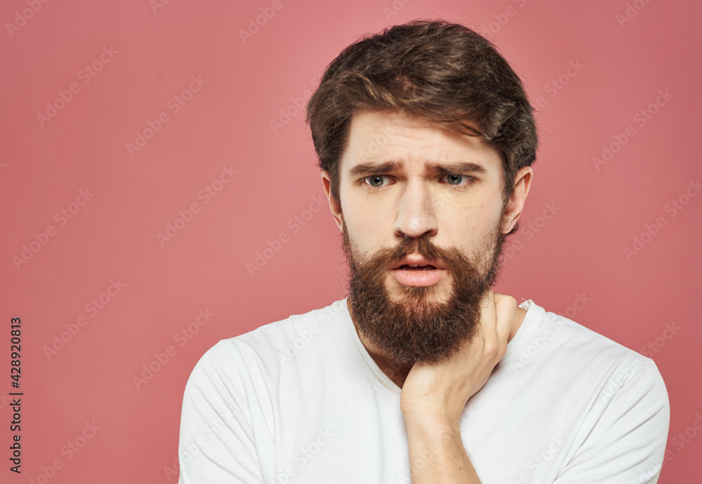 A man with a beard touches his face with his hand on a pink background A man with a beard touches his face with his hand on a pink background