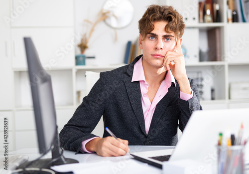 Upset attractive young businessman working documents and laptop in modern office