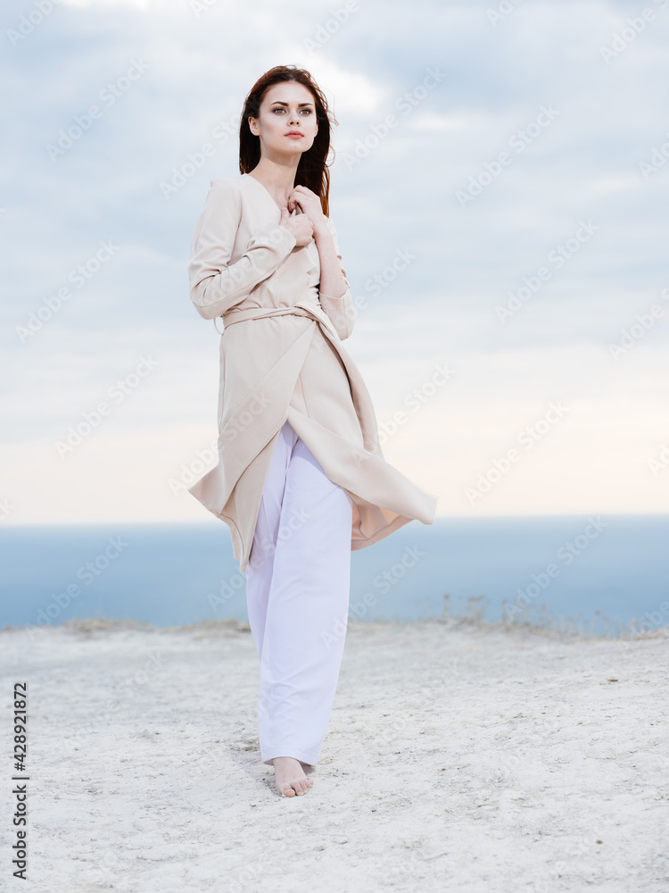 woman in light trousers and a sweater travels in the mountains on nature ocean in the background