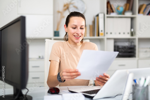 Girl business manager working in a large company examines the documentation on paper, sitting at the workplace in the ..office