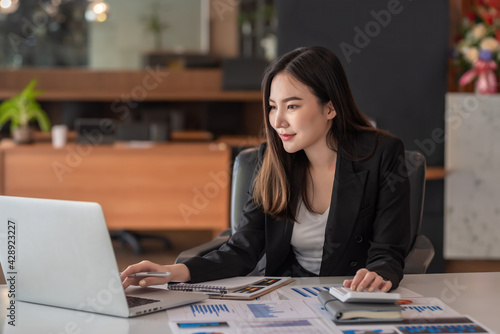 Beautiful Asian businesswoman analyzes charts using laptop calculator at the office. photo