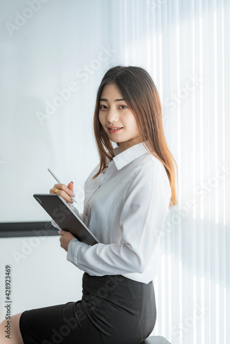 Confident Asian businesswoman sitting in a chair a holding digital tablet at the office. Looking at the camera.
