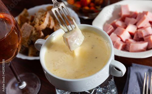 Delicate fondue from camembert with pieces of bread and sausages to dip into melted cheese served with wine