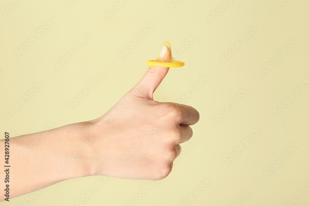 Female hand with condom showing thumb-up gesture on color background. Erotic concept Female hand with condom showing thumb-up gesture on color background. Erotic concept