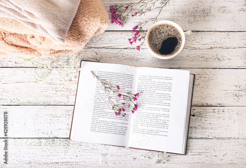 Book with fresh flowers and cup of coffee on table photo