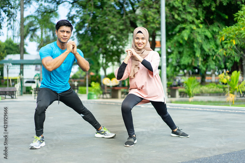 muslim couples in gym clothes doing the leg warm-up movement together before exercising in the park