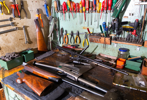 Workplace of gunsmith in professional weapons workshop with tools and disassembled shotgun during repair or maintenance