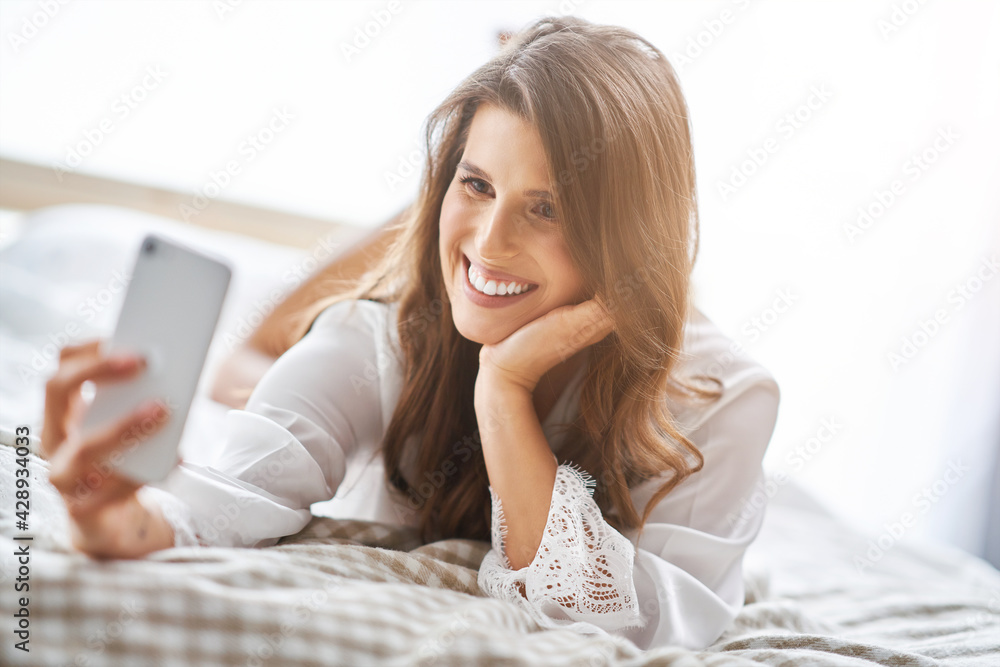 Happyadult woman using smartphone in bedroom in the morning Happyadult woman using smartphone in bedroom in the morning
