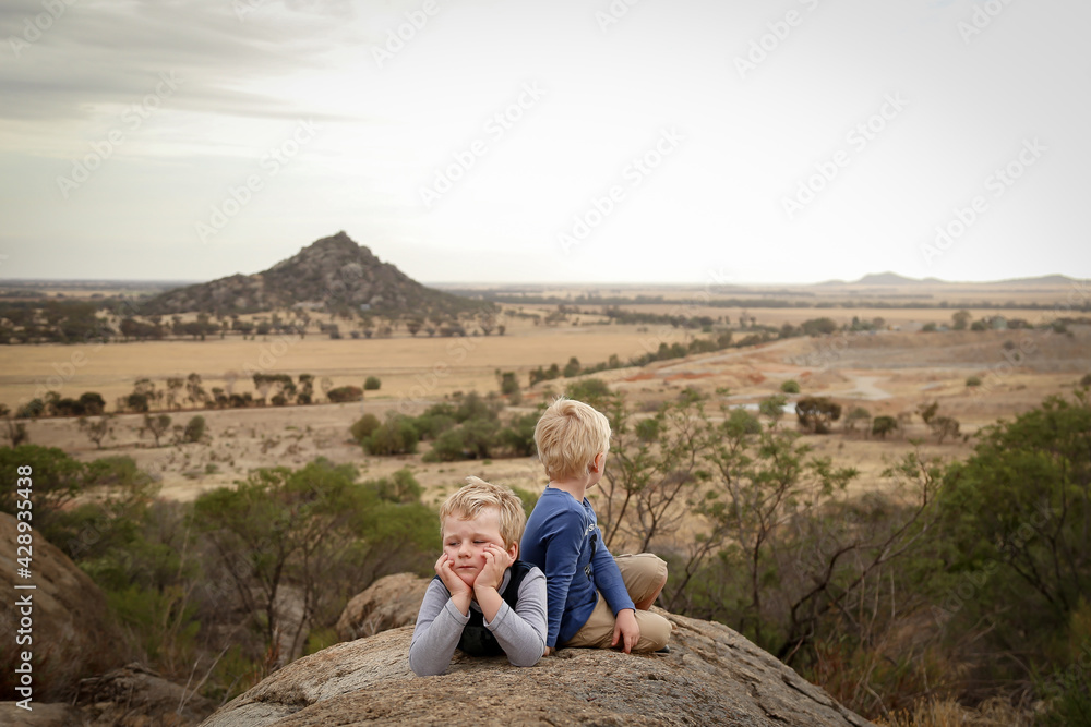 Little boys sitting on rock during bushwalk with view of Pyramid Hill, Victoria Australia in the background. Nature walk on a cloudy day.