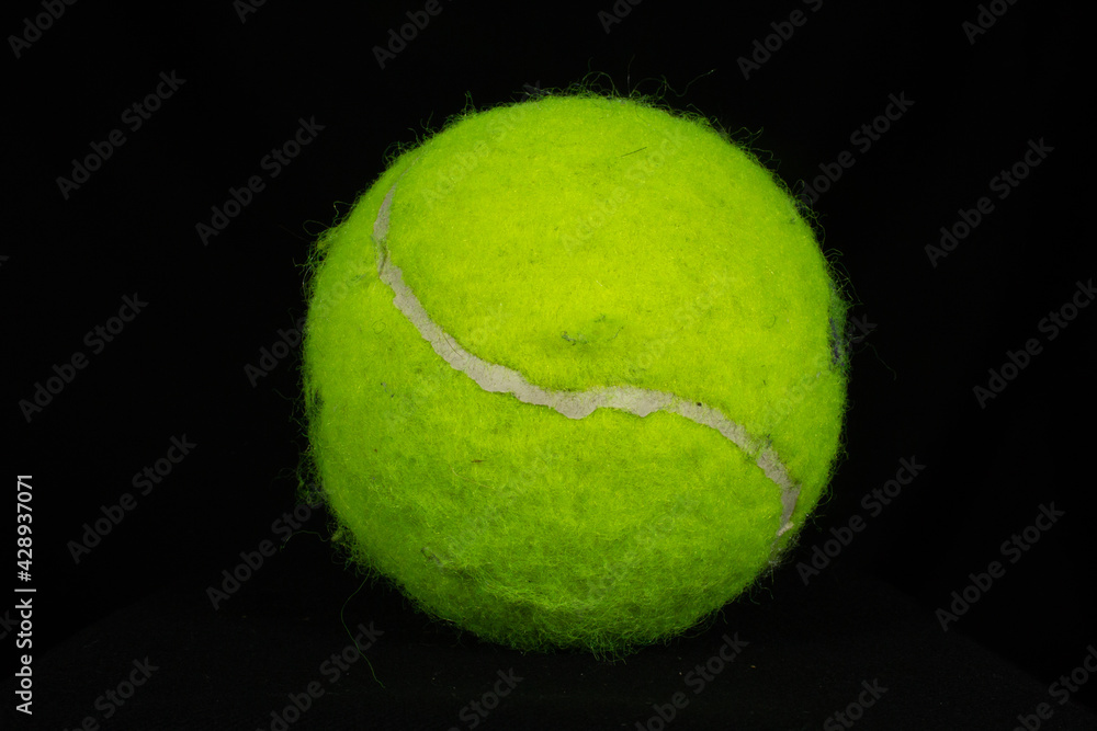 bright yellow tennis ball with dirt marks isolated on a black background