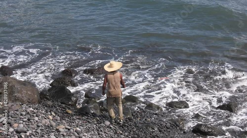 Un pêcheur sur le Barachois à l'île de La Réunion, l'homme lance sa ligne dans les vagues depuis une plage de cailloux