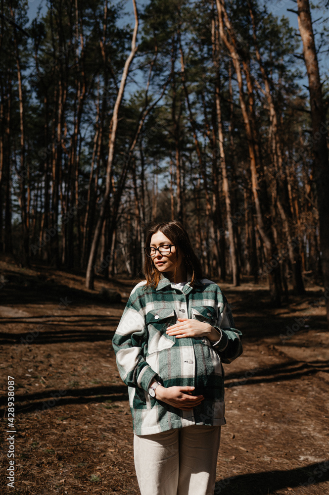 A pregnant woman in a shirt and white pants walks in the forest. A pregnant woman in a shirt and white pants walks in the forest.