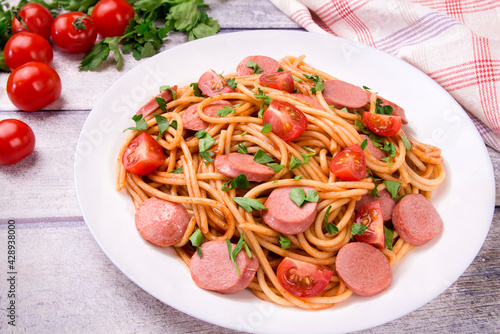 Pasta spaghetti with cherry tomatoes  fried sausage and parsley  in white plate on a light background.