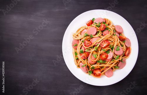 Pasta spaghetti with cherry tomatoes, fried sausage and parsley in white plate on a black background.