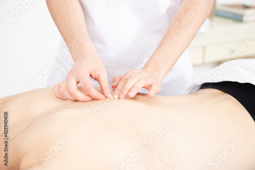 Closeup view of a physiotherapist exploring the backbone or dorsal spine of a shirtless patient.