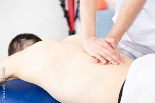 Closeup view of a physiotherapist treating the mobility of the backbone or dorsal spine of a shirtless patient.
