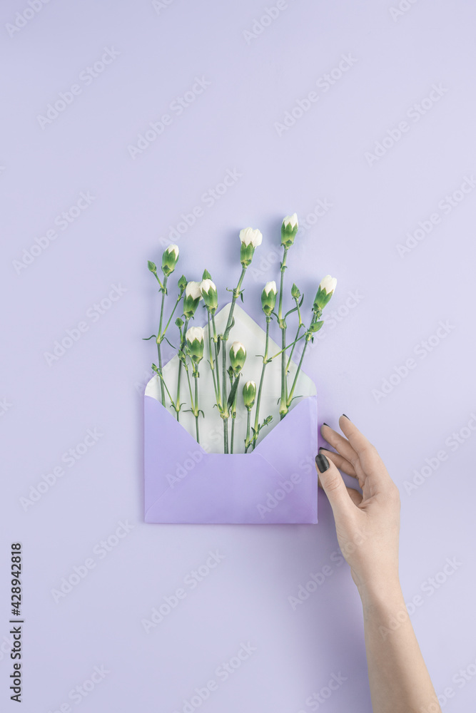 Φωτογραφία Minimal newsletter email concept with hand holding a violet envelope with white summer flowers on bright purple background