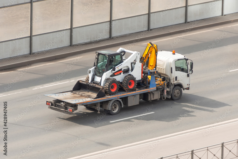 Transportation of a mini tractor by a tow truck.