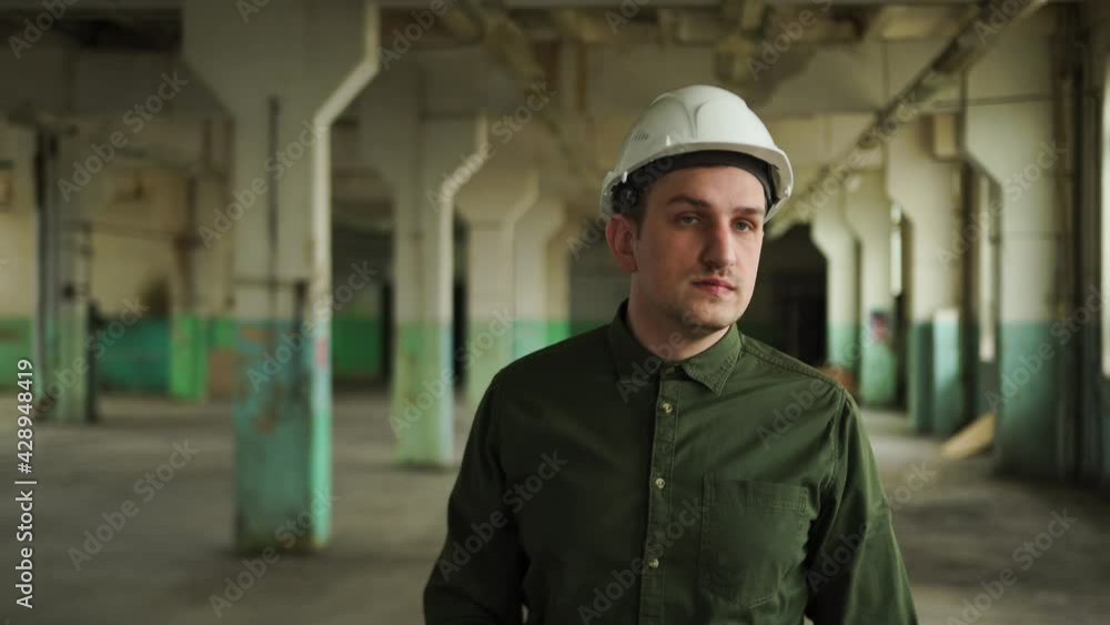 Engineer manager puts white helmet head. Walks through large hall columns supports, construction site, looks around, checks work contractors, evaluates investments. Demolition, reconstruction building Engineer manager puts white helmet head. Walks through large hall columns supports, construction site, looks around, checks work contractors, evaluates investments. Demolition, reconstruction building